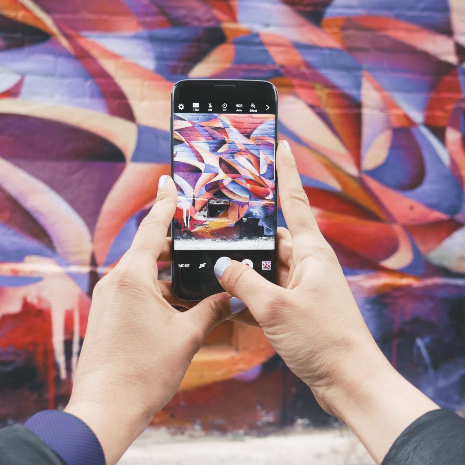 Person taking a photo of vibrant street art with a smartphone, showcasing creative content for social media marketing with RevampX.